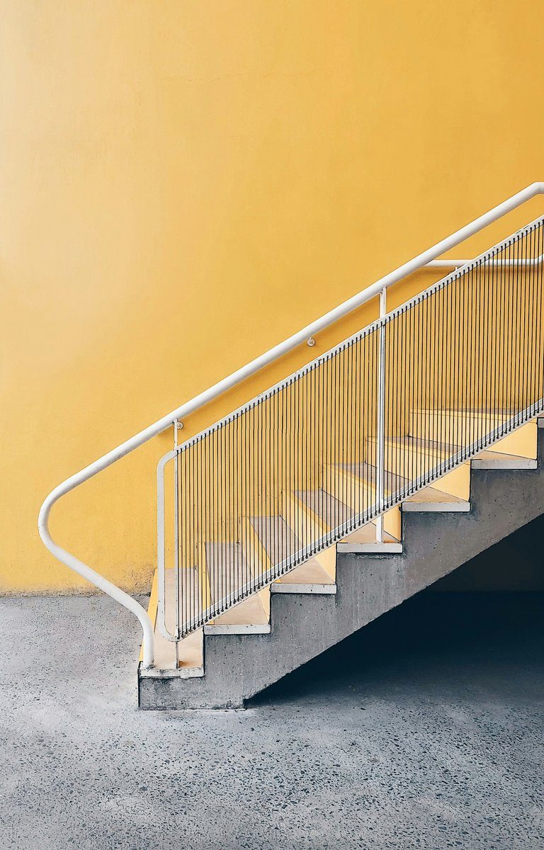 Escalier en béton avec une rampe métallique blanche devant un mur jaune