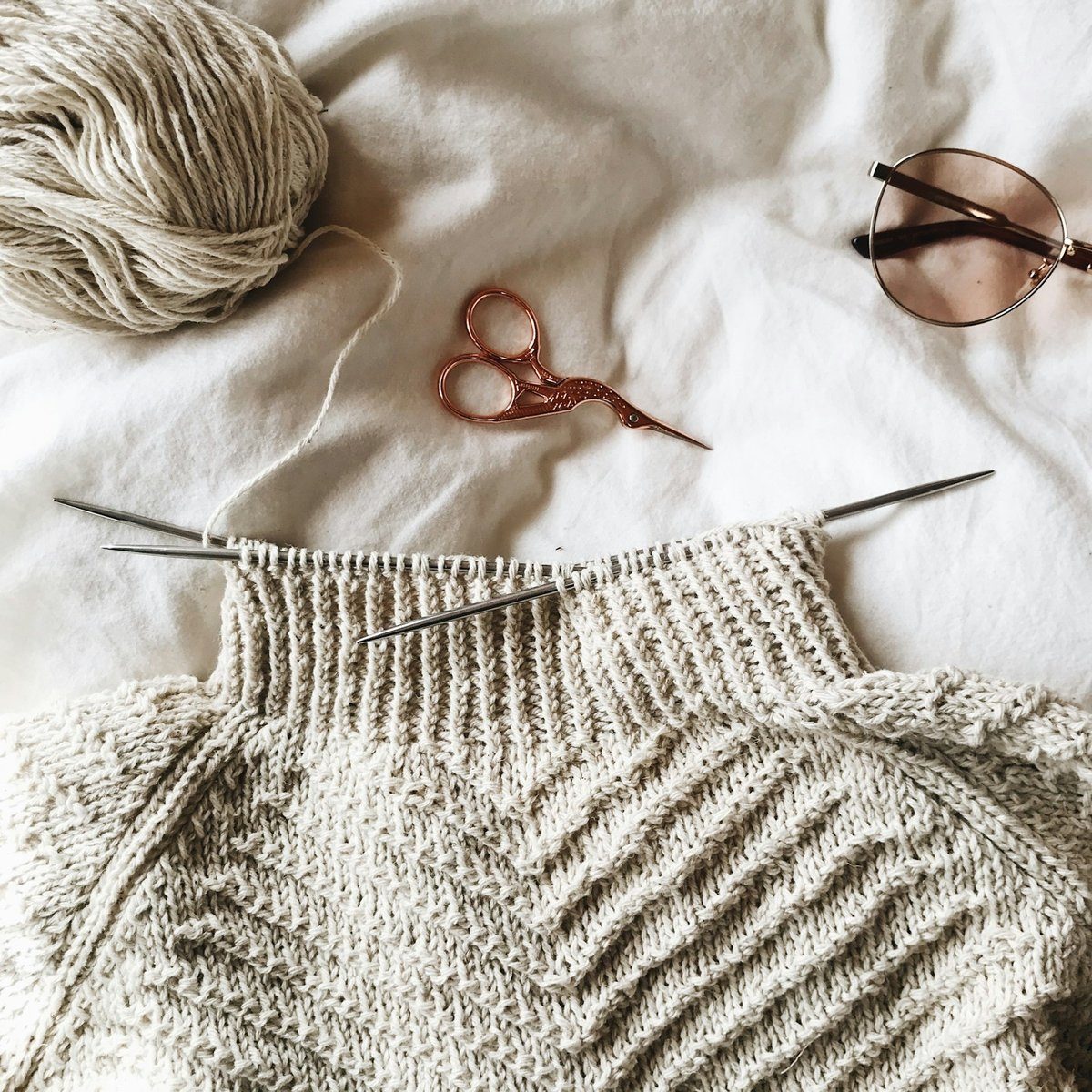 Tricot en cours, pelote de laine, ciseaux et lunettes sur un drap